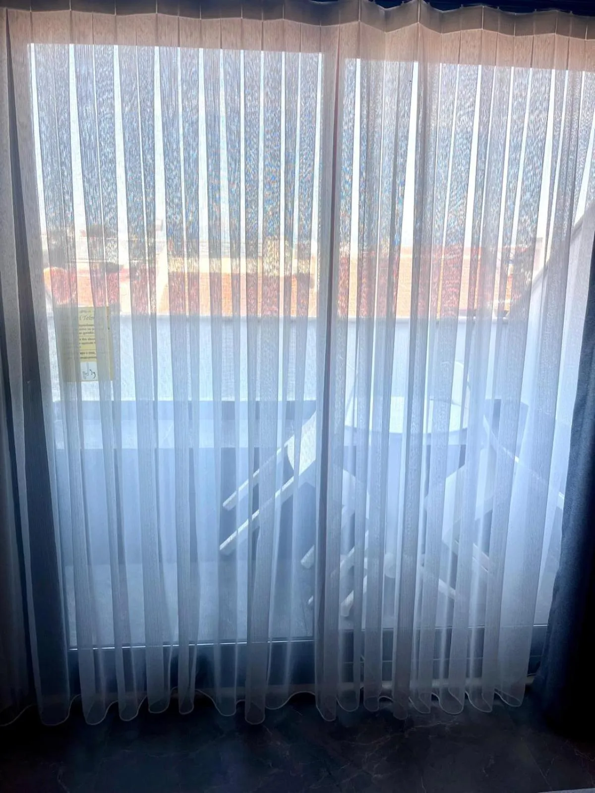 Rideaux blancs laissant entrevoir une vue extérieure floue.