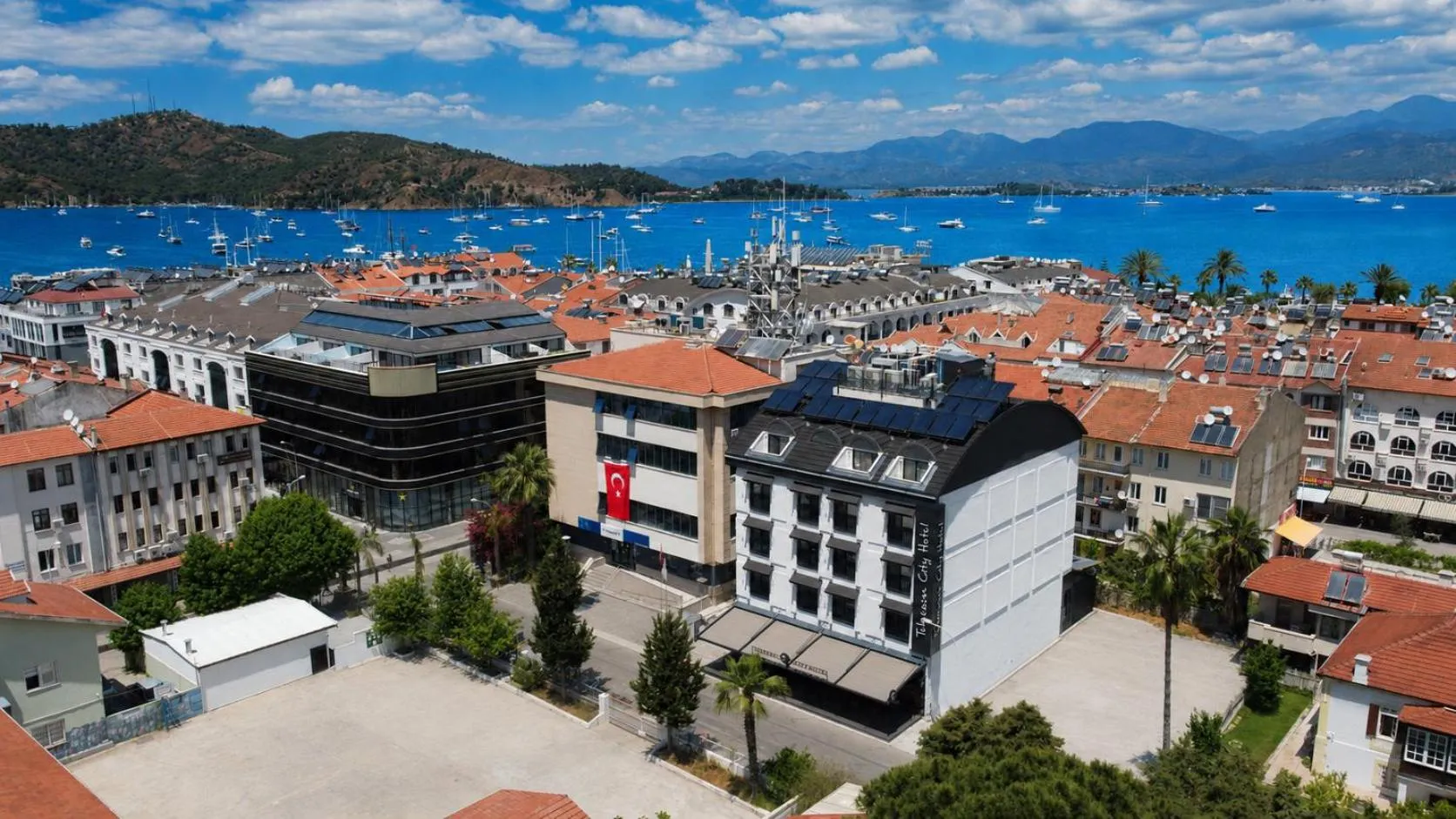 Vue aérienne d'une ville côtière avec des bâtiments aux toits rouges et une baie ensoleillée.