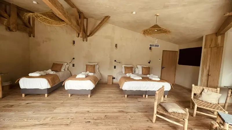 Une chambre lumineuse avec trois lits simples et un fauteuil en osier.