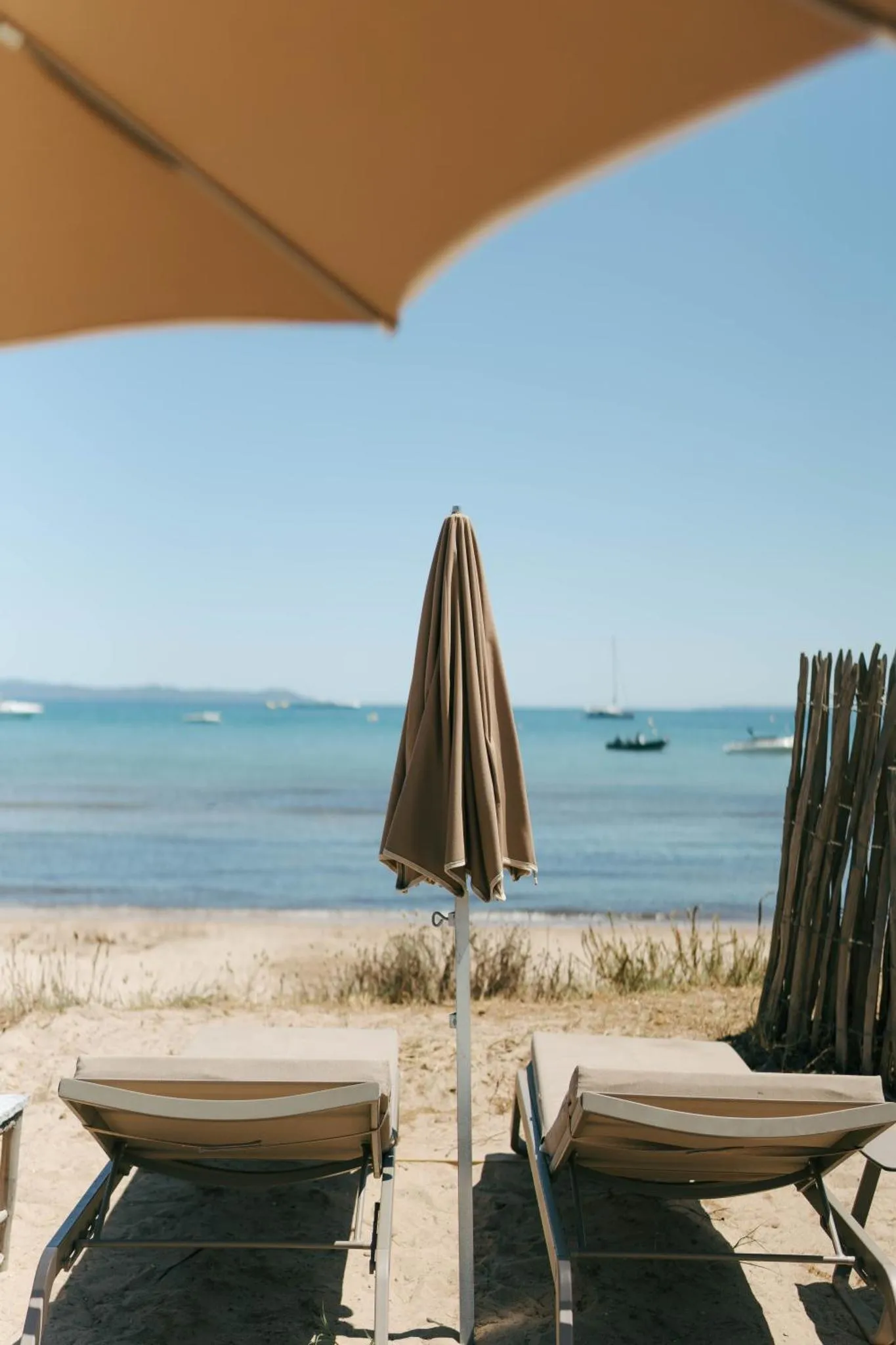 Deux transats sur une plage de sable fin, avec parasols et vue sur la mer.