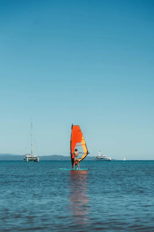 Un pratiquant de planche à voile glisse sur une mer calme sous un ciel bleu.
