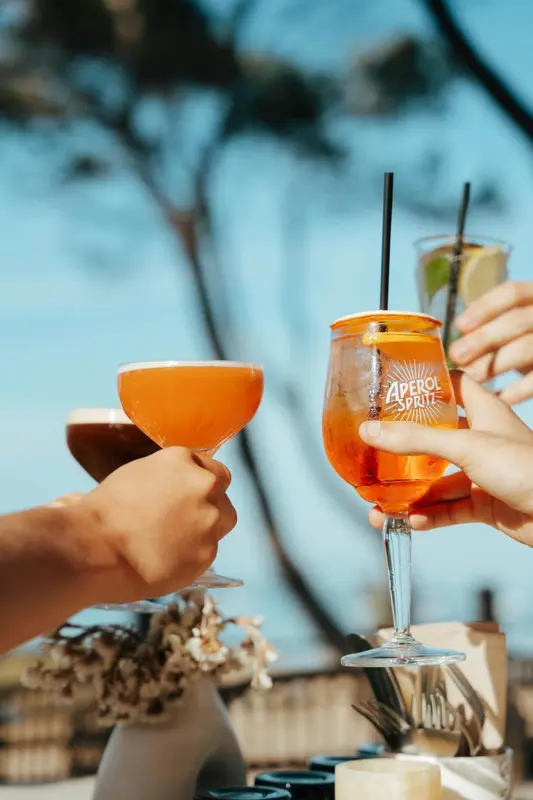 Des verres colorés sont levés dans un toast sur une terrasse ensoleillée.