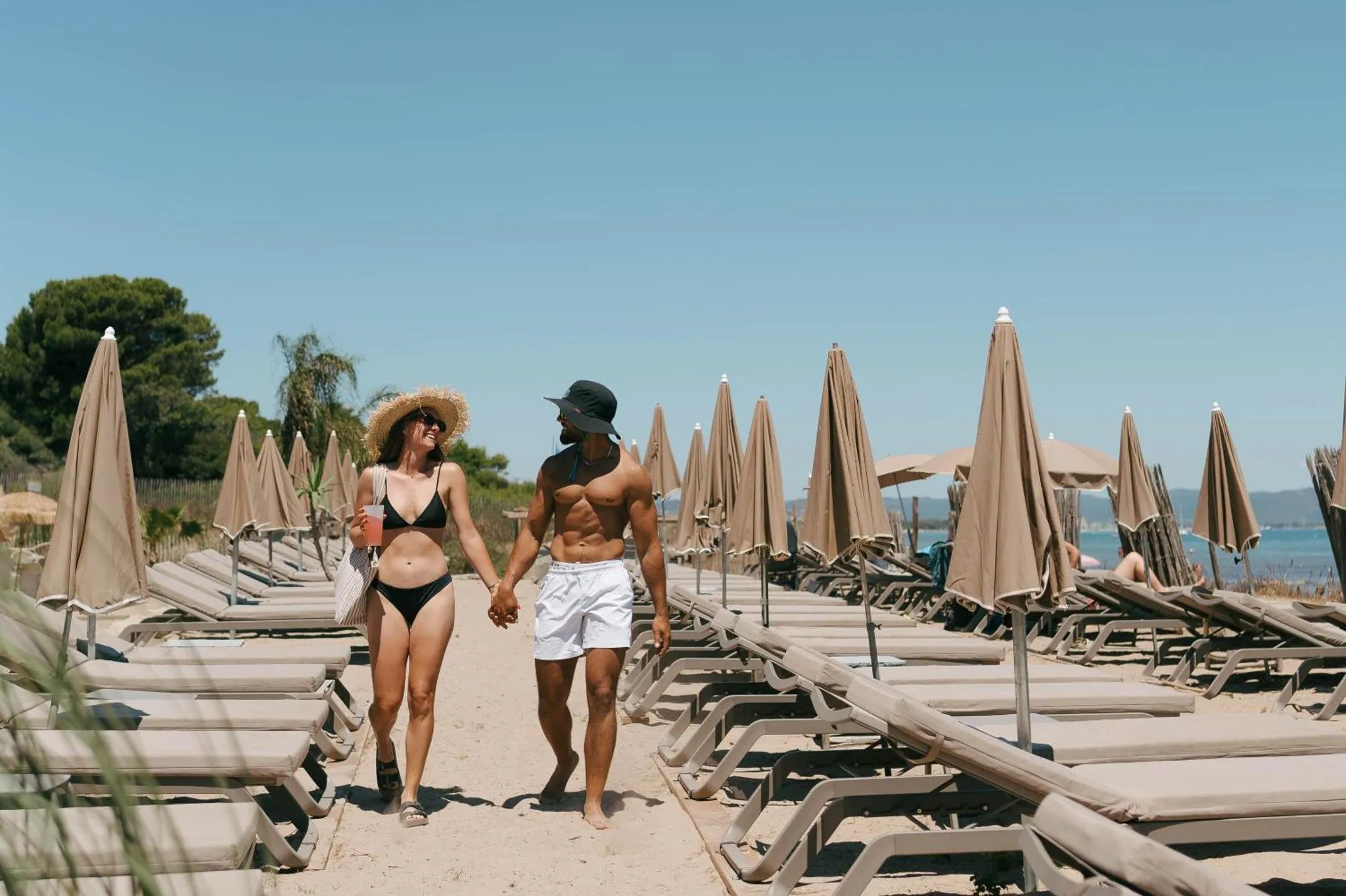 Un couple se promène sur une plage de sable fin bordée de transats et de parasols.