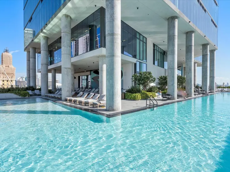 Une piscine turquoise bordée de transats, avec une vue sur la ville.