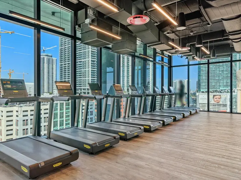 Une salle de sport lumineuse avec plusieurs tapis de course face à une vue urbaine.