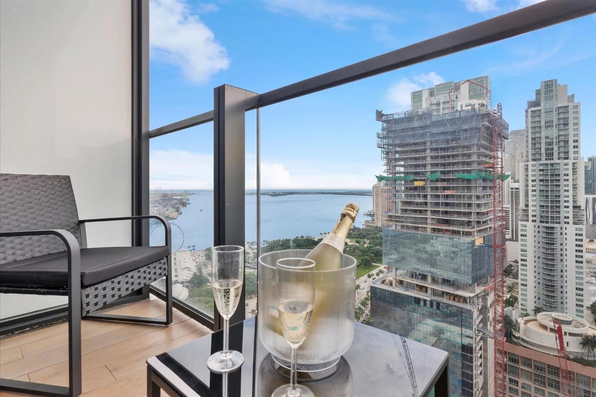 Une bouteille de champagne et des verres sur une table basse sur une terrasse avec vue sur la mer et la ville.
