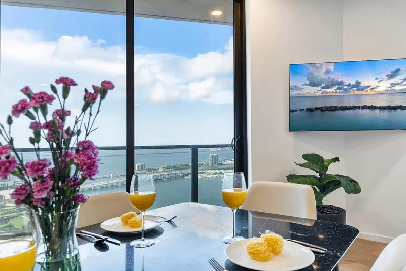 Une table est dressée devant une grande fenêtre avec vue sur la mer et la ville.