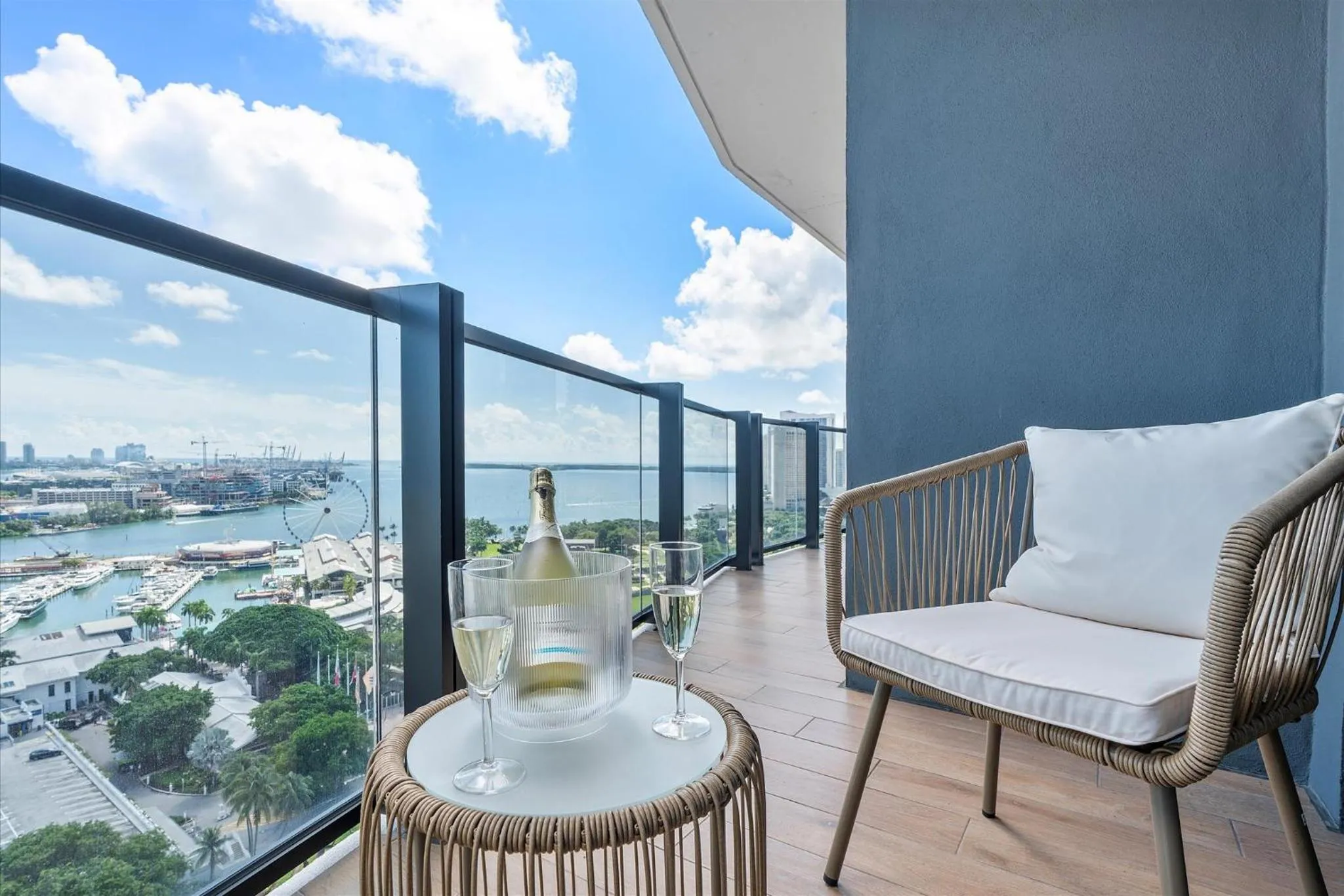 Une bouteille de champagne et deux verres sur une table basse en osier sur une terrasse avec vue sur la mer.