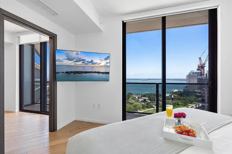 Une chambre lumineuse avec un grand lit donnant sur une vue urbaine et maritime.