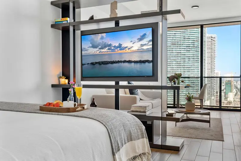 Une chambre avec un grand lit et un espace salon avec télévision face à une vue urbaine.