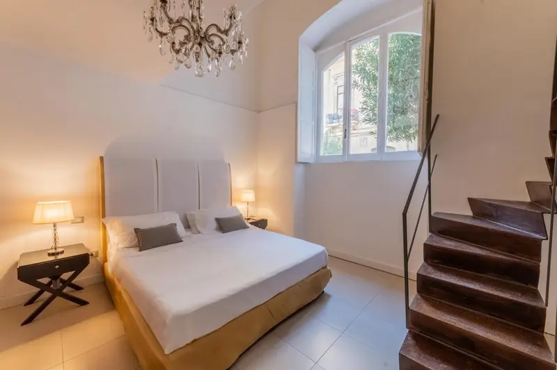 Une chambre lumineuse avec un grand lit et un escalier en bois.