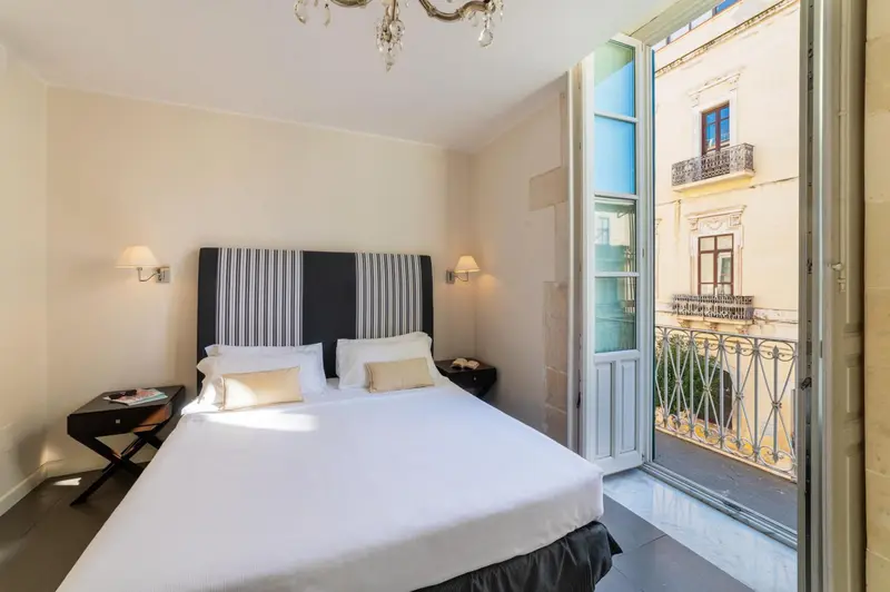 Une chambre lumineuse avec un grand lit et un balcon ouvert.