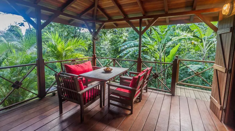 Terrasse en bois avec table et chaises rouges, entourée d'une végétation luxuriante.