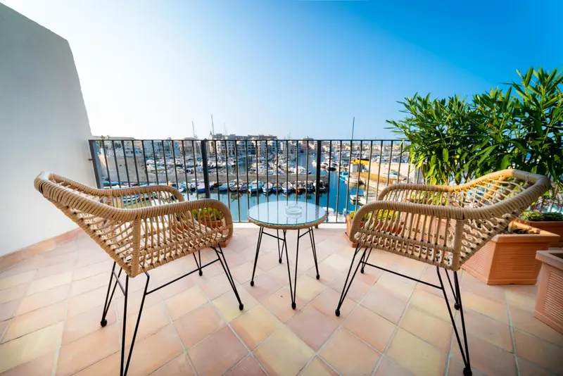 Terrasse aménagée avec mobilier en rotin donnant sur un port de plaisance ensoleillé.