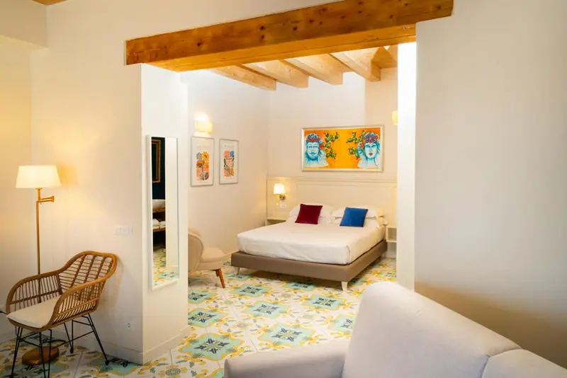 Une chambre lumineuse avec un lit et un fauteuil en rotin.