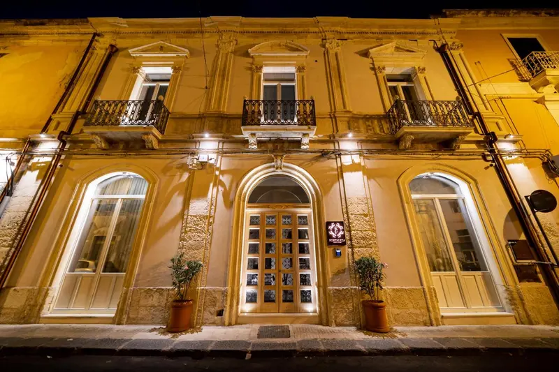 Façade d'un bâtiment illuminé la nuit avec des fenêtres et une entrée.