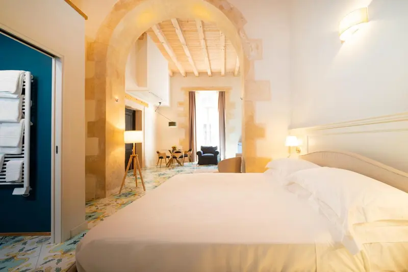 Une chambre lumineuse avec un lit fait et un mur en pierre.