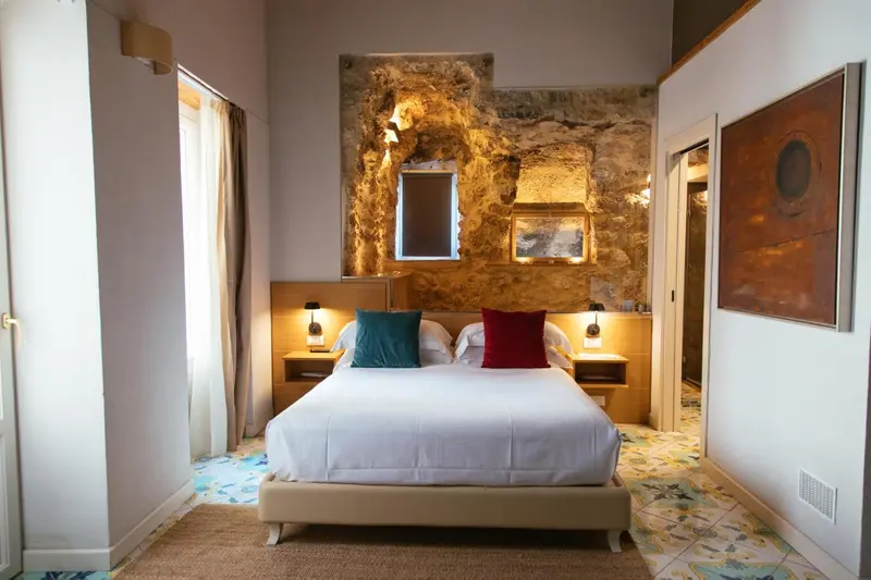 Une chambre lumineuse avec un lit double et un mur en pierre apparente.