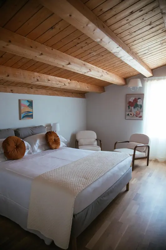 Une chambre lumineuse avec un lit fait et deux fauteuils.