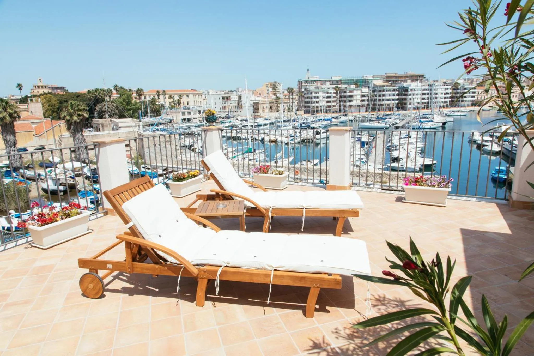 Deux transats blancs sur une terrasse ensoleillée avec vue sur un port de plaisance.