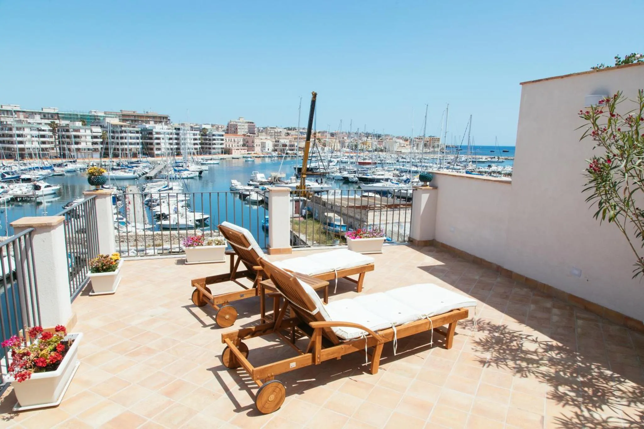 Deux transats sur une terrasse ensoleillée donnant sur un port de plaisance.