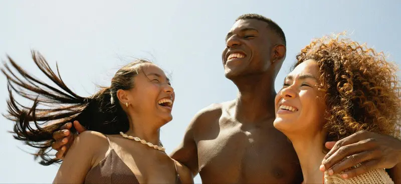 Trois personnes sourient en regardant vers le haut, les cheveux au vent.