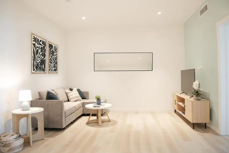 Un salon clair avec un canapé d'angle et un meuble bas pour la télévision.