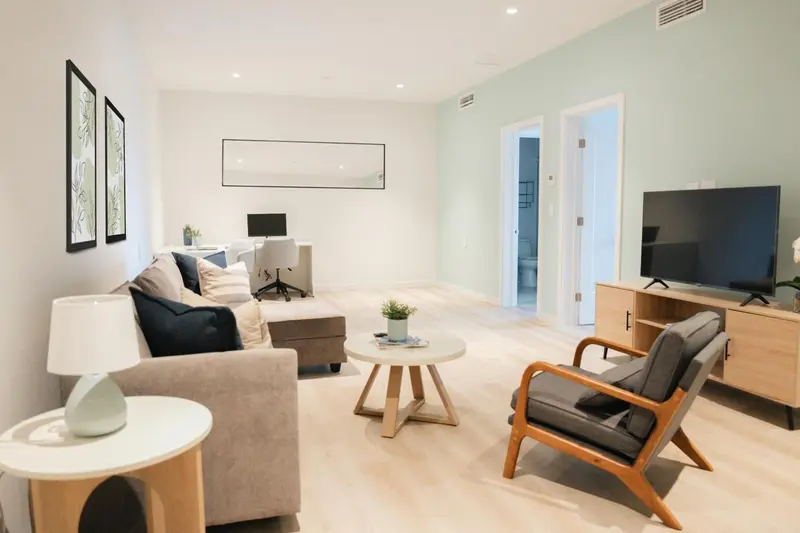 Un salon clair avec canapé, fauteuil et télévision.