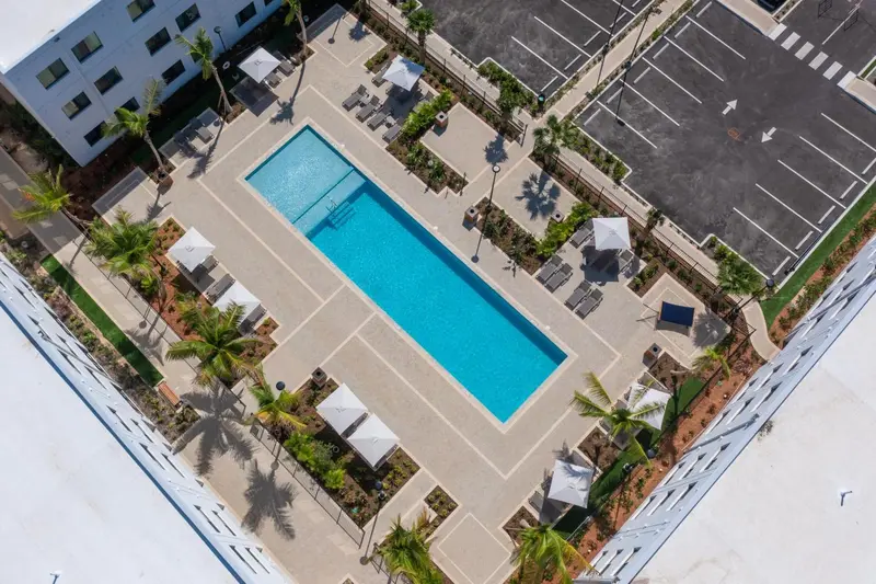 Vue aérienne d'une piscine rectangulaire entourée de chaises longues et de végétation tropicale.
