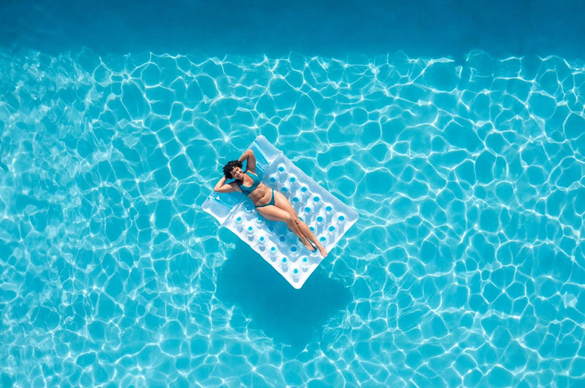 Une personne se relaxe sur un matelas flottant dans une piscine turquoise.