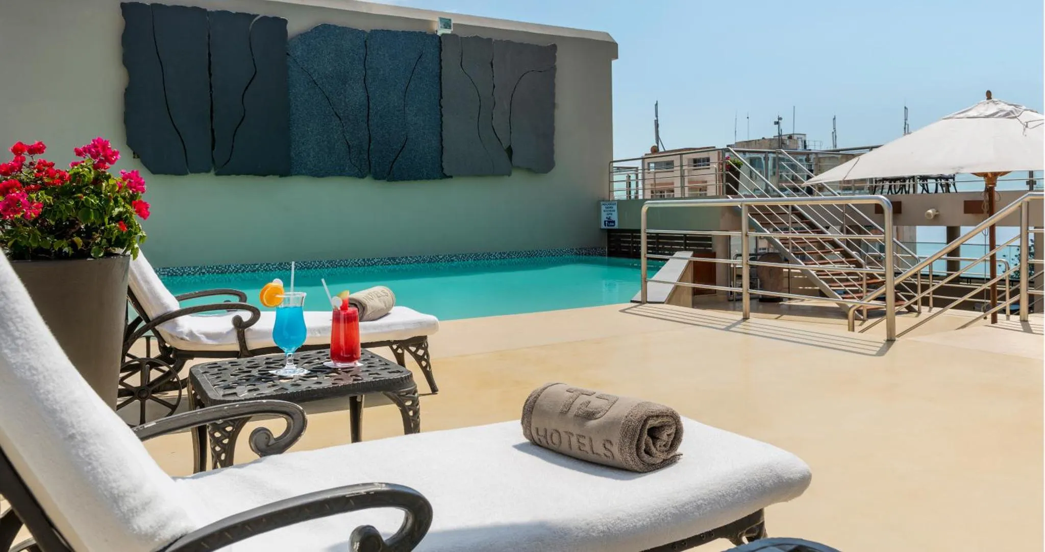 Transats et cocktails au bord d'une piscine sur une terrasse ensoleillée.