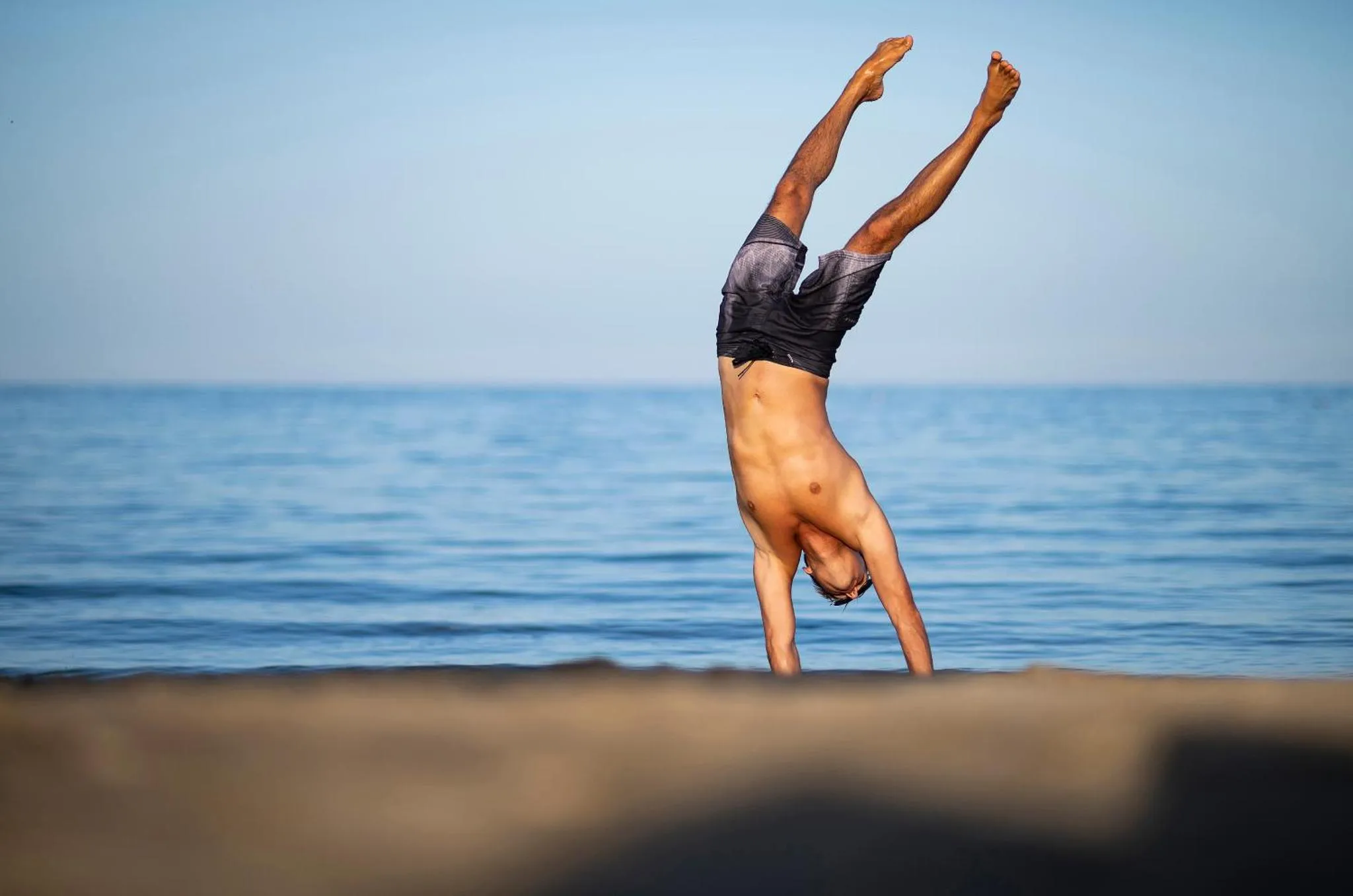 Un homme fait une roue sur une plage de sable fin face à la mer.