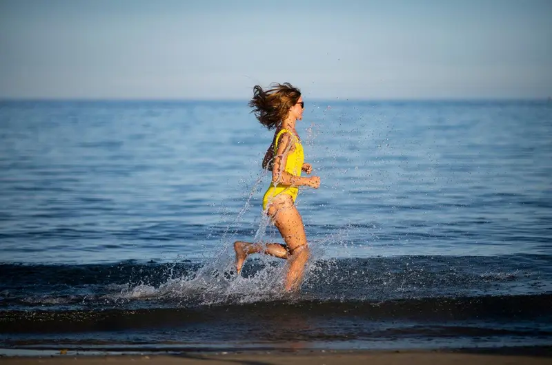 Une personne court dans les vagues sur une plage ensoleillée.