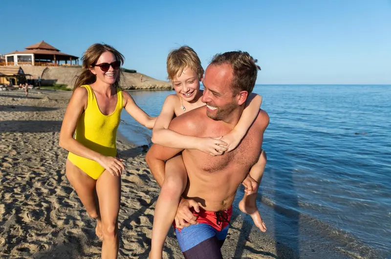 Une famille s'amuse sur une plage de sable fin, avec la mer en arrière-plan.