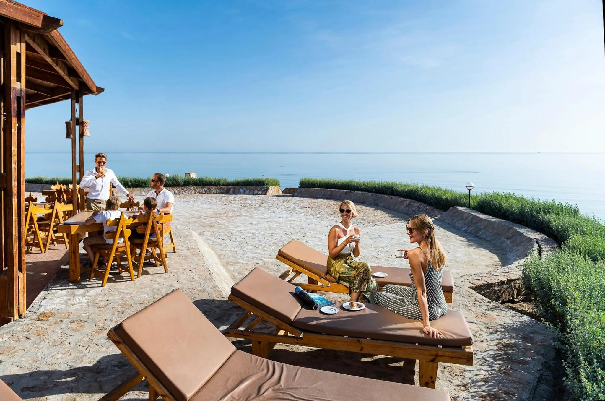 Une terrasse ombragée avec des transats et des tables de repas offre une vue sur la mer.