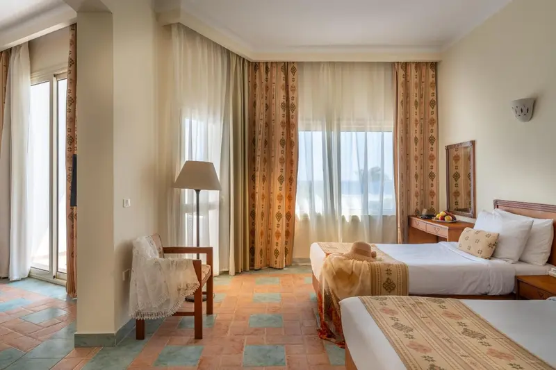 Chambre lumineuse avec un lit et un fauteuil près d'une fenêtre.
