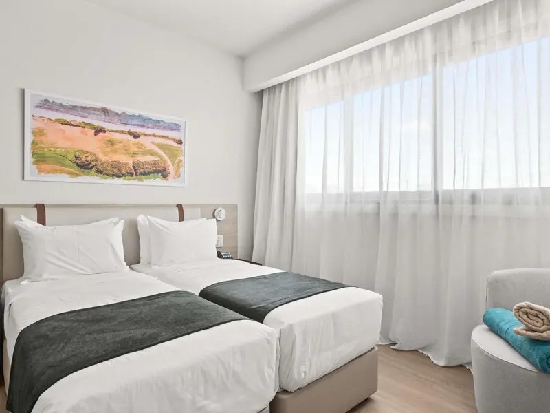 Une chambre lumineuse avec deux lits simples et un tableau au mur.