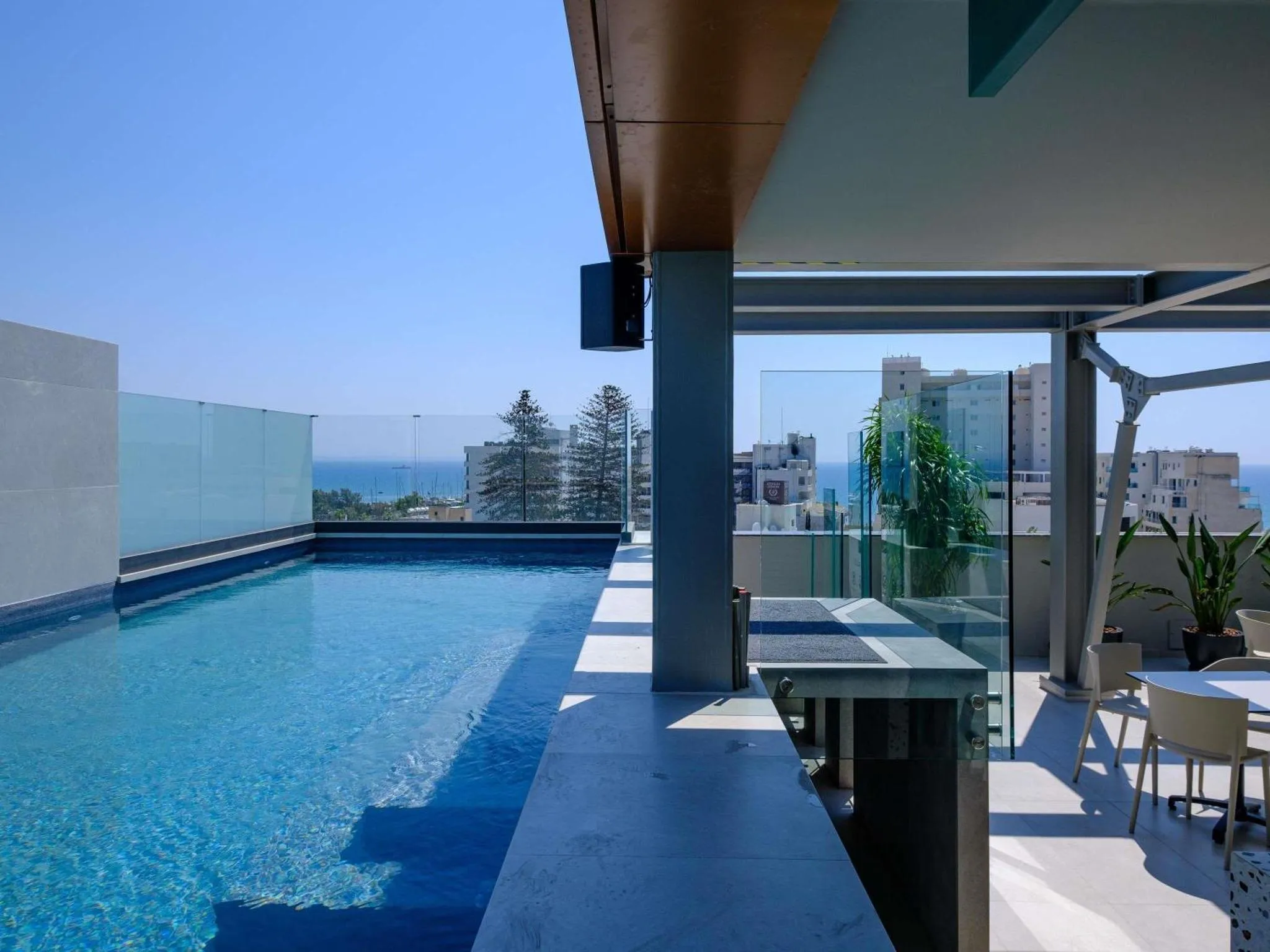 Une piscine rectangulaire avec une terrasse ensoleillée et une vue sur la mer.