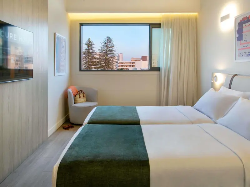 Une chambre lumineuse avec un lit double et un fauteuil près d'une fenêtre.