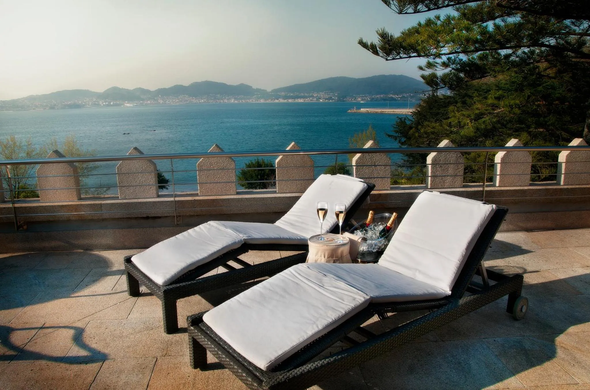 Deux transats blancs avec des boissons sur une terrasse ensoleillée avec vue sur la mer.