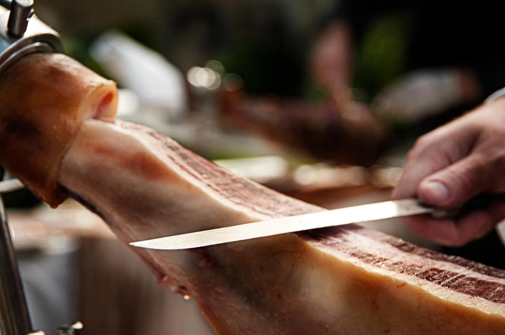 Une main tranche du jambon cru avec un couteau.