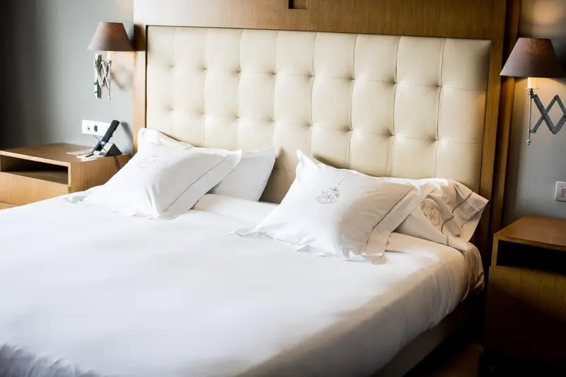 Un lit double avec des oreillers blancs et une tête de lit capitonnée.