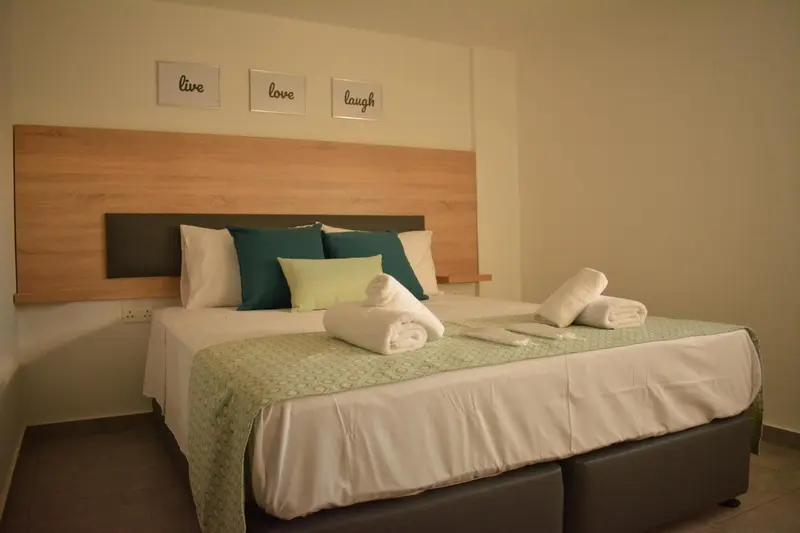 Une chambre lumineuse avec un grand lit recouvert d'une couette verte et de coussins.