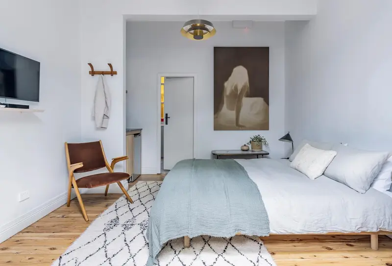 Une chambre lumineuse avec un lit fait et un fauteuil en cuir.