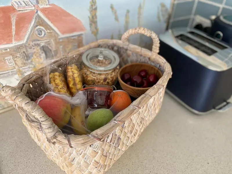 Un panier garni de fruits, viennoiseries et confitures est présenté sur un plan de travail.