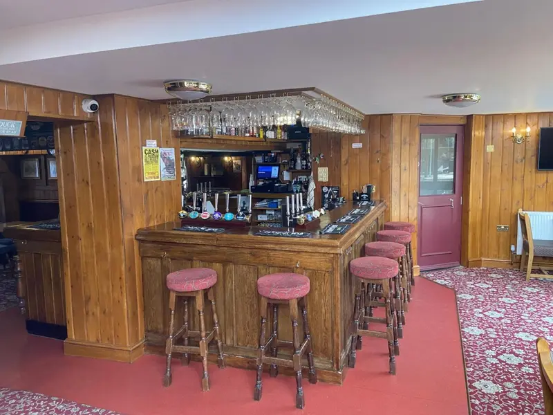 Un comptoir de bar en bois avec des tabourets et des bouteilles exposées.