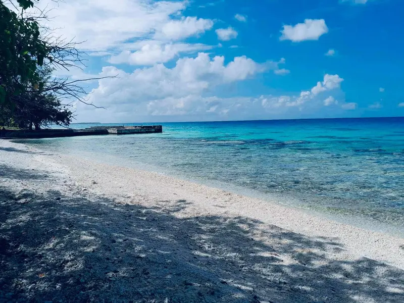 Une plage de sable blanc borde une mer turquoise sous un ciel nuageux.