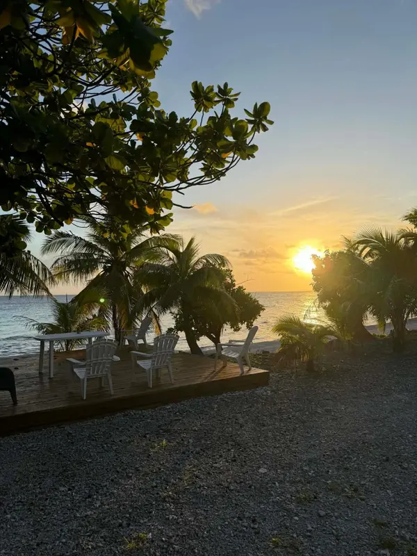 Une terrasse en bois avec des chaises et une table face à la mer au coucher du soleil.