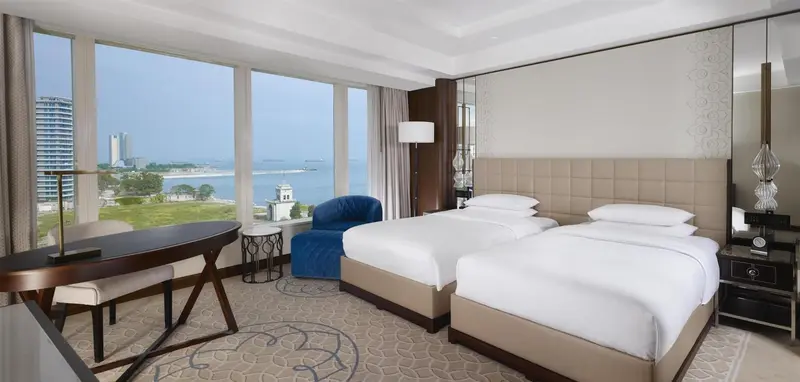 Chambre lumineuse avec deux lits simples et vue sur la mer.