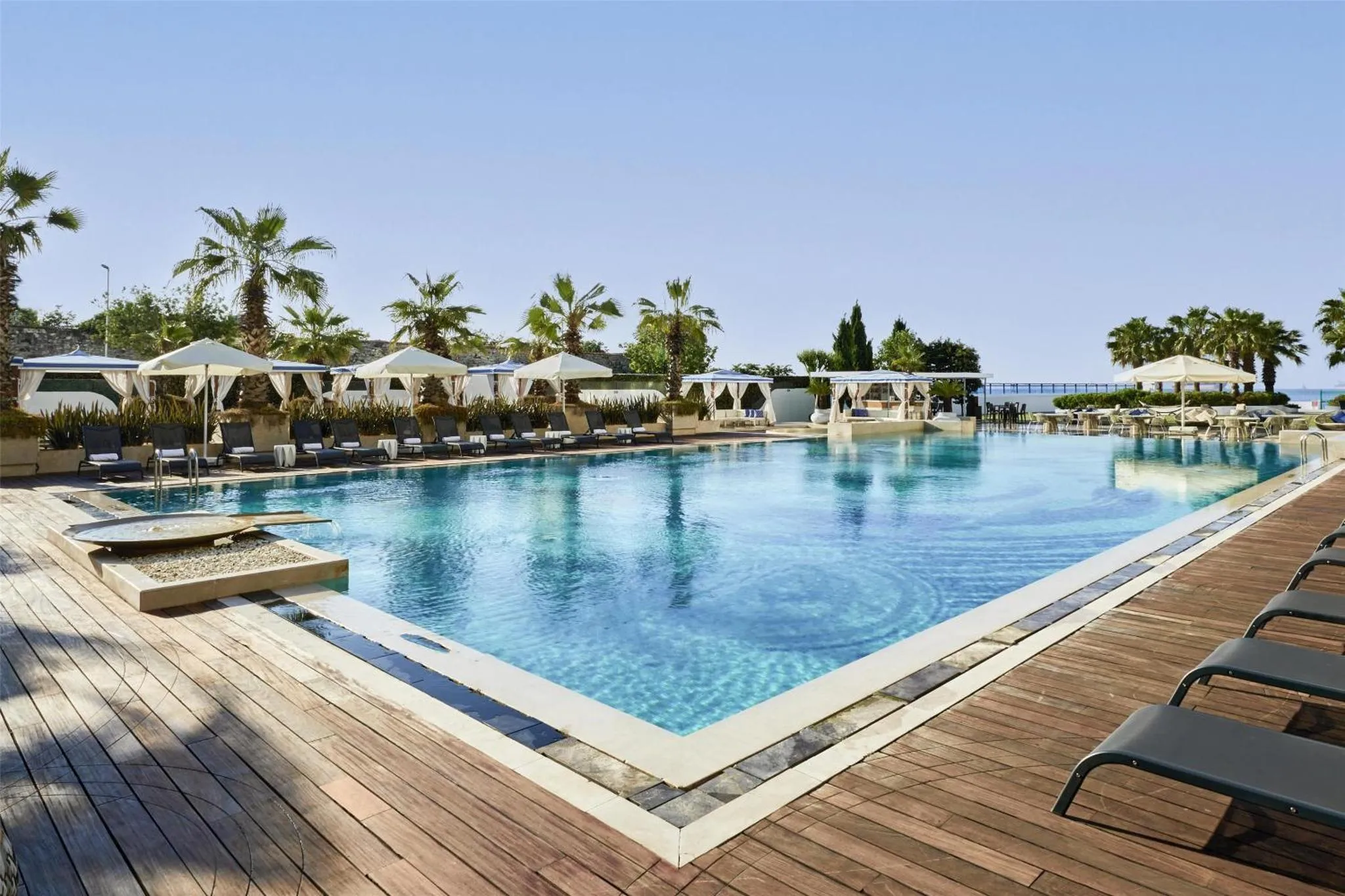 Une grande piscine rectangulaire bordée d'une terrasse en bois et de transats.